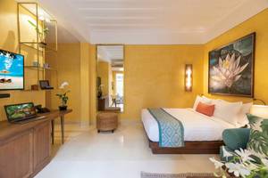 Innenansicht eines Zimmers im Buri Rasa Village Samui mit gelben Wänden, einem Bett, Schreibtisch und Laptop.