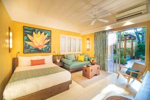 Ein hellgelbes Zimmer im Buri Rasa Village Samui Hotel mit einem Bett, Sofa, Tisch und Gartenblick.