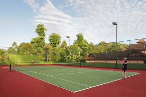 Tennisplatz im Freien im Khao Lak Merlin Resort mit zwei Spielern und umliegenden Bäumen.