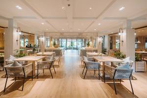 Innenbereich des Khao Lak Merlin Resorts mit hölzernen Tischen, Stühlen und Pflanzen.