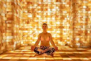 Frau in Meditationshaltung in einem Raum mit Wänden aus rosa Steinfliesen