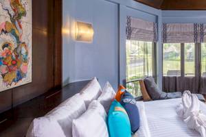 Hotelzimmer im Peace Laguna Resort & Spa mit blauen Wänden, Fenstern, einem Bett, Kissen und einem Ausblick auf einen See.