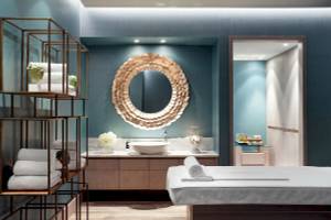 Wellnessbereich im Ikos Aria Hotel mit runden Spiegel, weißen Handtüchern und einer Tischlampe.