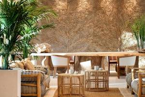 Ein Hotel-Loungebereich mit einem langen Holztisch, umgeben von Stühlen und Pflanzen.