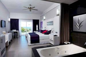 Suite im Riu Palace Costa Rica mit Jacuzzi, Bett, Fernseher und Ausblick.