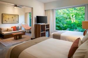 Hotelzimmer im El Mangroove Autograph Collection mit zwei Betten, Fernseher, Sofa und Aussicht auf den Garten.