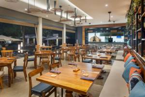 Innenansicht des Restaurants im El Mangroove, Autograph Collection mit Holztischen, Stühlen und einer Bar.