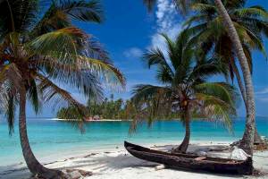 Strand mit altem Boot unter Palmen und blauem Himmel