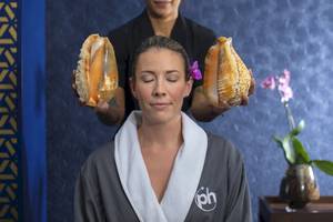 Frau im Hotel, die sich von jemandem mit großen Schneckenhörnern auf den Kopf massieren lässt.