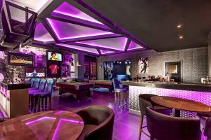 Innenansicht der Poolbar im Planet Hollywood Beach Resort mit violetten Beleuchtung, Billardtischen und Bar.
