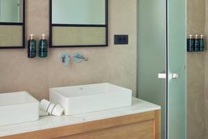 Badezimmer im Melia Durres Albania Hotel mit zwei Waschbecken, Spiegeln und Dusche.