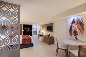 Innenansicht eines Hotelzimmers im Emotions By Hodelpa Puerto Plata, mit Bett, Schreibtisch und Kunstwerk.