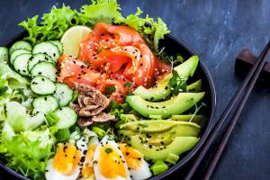 Ein Salat mit Salatblättern, Gurkenscheiben, Lachs, Avocado und Eiern in einer Schüssel.