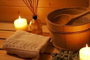 Eine Sauna mit einer Holzbadewanne, einem Holzlöffel, zwei Kerzen und einem Handtuch.