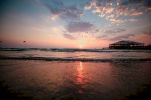 Sonnenuntergang am Strand mit einem Pavillon im Hintergrund und roten Fahnen im Wasser