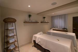 Massageraum im Emotions By Hodelpa Hotel mit zwei Massagetischen und einer Holzregal.