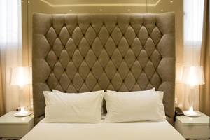 Hotelbett mit gepolstertem Kopfteil, weißen Kissen und Nachttischen mit Lampen.