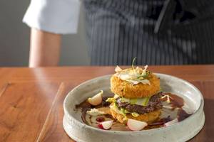 Ein Burger in einer Schale mit Rotkohlscheiben und Sauce auf einem Holztisch.