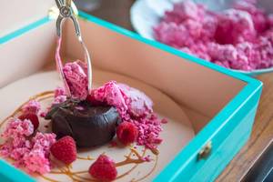Ein Schokoladen-Dessert in einer blauen Schachtel mit rosa Eis und Himbeeren.