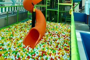 Ein Kinderspielplatz mit einer orangefarbenen Ballenrutsche, umgeben von bunten Bällen.