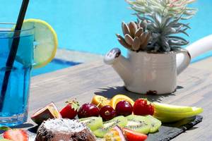 Dyrrah Hotel Poolseite mit einem Glas blauem Getränk, einer Zitronenscheibe, einer Obstplatte und einem Topf mit Sukkulenten neben dem Pool.