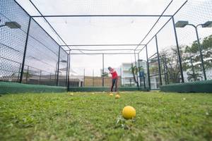Golftraining unter einem Netz auf einem gepflegten Rasen.