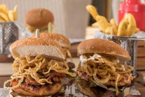 Hühnchenburger mit gebratenen Zwiebeln und Pommes frites auf einer Holzplatte.