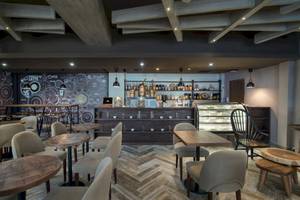 Innenansicht des Cafés im Emotions By Hodelpa Hotel in Puerto Plata mit Tischen, Stühlen und Theke.