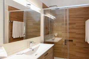 Badezimmer im Pedras da Rainha Resort mit holzvertäfelten Wänden, einer Glasdusche und einem Waschbecken.