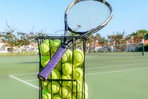 Korb voller Tennisbälle auf einem Tennisplatz im Freien