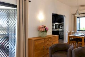 Innenansicht des Pedras da Rainha Resorts mit Esstisch, Blumenvase, Schrank und Küche im Hintergrund.
