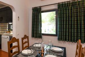 Esszimmer im Pedras da Rainha Resort mit Tisch, Stühlen, Geschirr und Fenster mit grünen Vorhängen.