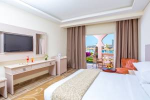 Innenansicht eines Hotelzimmers im Pickalbatros Aqua Vista Resort mit einem Bett, Fernseher, Schreibtisch und Balkon.