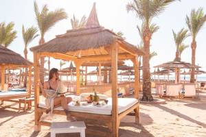 Frau sitzt auf einem Bett unter einem Hutdach am Strand
