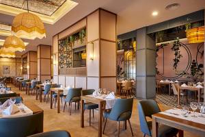 Innenansicht des Restaurants im RIU Palace Macao mit gedeckten Tischen und Stühlen, dekorativen Lampen und Pflanzen.