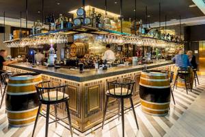 Bar im Al Bandar Rotana Hotel mit Holzfässern und Hockern.
