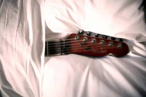 Der Hals einer roten Gitarre liegt auf einem weißen Laken.