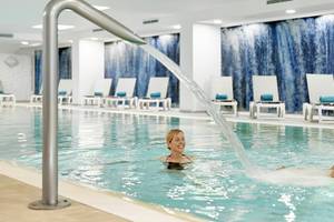 Ein Schwimmbad im Iberostar Cristina Hotel mit Wasserfall und zwei Personen, die darin schwimmen.