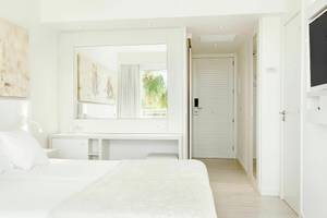 Innenansicht eines Schlafzimmers im Iberostar Cristina Hotel mit weißem Bett, Möbeln und Dekoration.