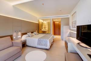 Innenansicht eines Hotelzimmers im Hipotels Gran Playa de Palma, mit Bett, Sofa, Fernseher und modernem Badezimmer.