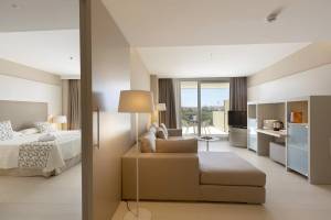 Innenansicht der Suite im Hipotels Gran Playa de Palma mit Bett, Sofa, Fernseher und Balkon.