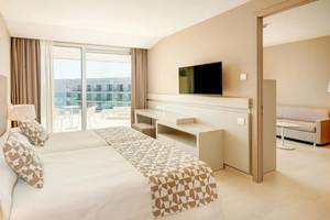Innenansicht eines Hotelzimmers im Hipotels Gran Playa de Palma mit Doppelbett, Fernseher, Sofa und Terrassenblick.