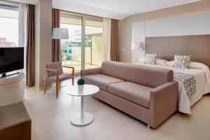 Innenansicht der Suite im Hotel Hipotels Gran Playa de Palma mit Bett, Sofa, Tisch und Fernseher.