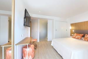 Innenansicht eines Schlafzimmers im Iberostar Playa de Muro Hotel mit weißem Bett, orangen Kissen und moderner Einrichtung.