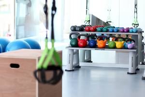 Fitnessstudio mit verschiedenen Gewichten und Trainingsgeräten auf einem Regal.