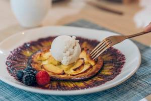 Ein Teller mit Apfelkuchen, Eis und Beeren auf einem blauen Tischtuch.