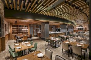 Innenansicht des Restaurants im Titanic Luxury Collection Bodrum Hotel mit Holztischen, Stühlen und einem offenen Bereich mit einer Bar.