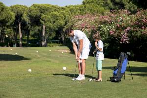 Ein Mann und ein Kind spielen Golf auf einem Golfplatz mit Bäumen und Blumen im Hintergrund.