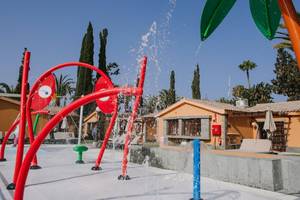 Außenbereich des Pools im Suites & Villas By Dunas Hotel mit bunten Wassersprudlern und Gebäuden im Hintergrund.