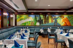Innenansicht des Restaurants im Xanadu Resort Hotel mit einer großen Wandmalerei, blauen Sitzbankreihen und gedeckten Tischen.